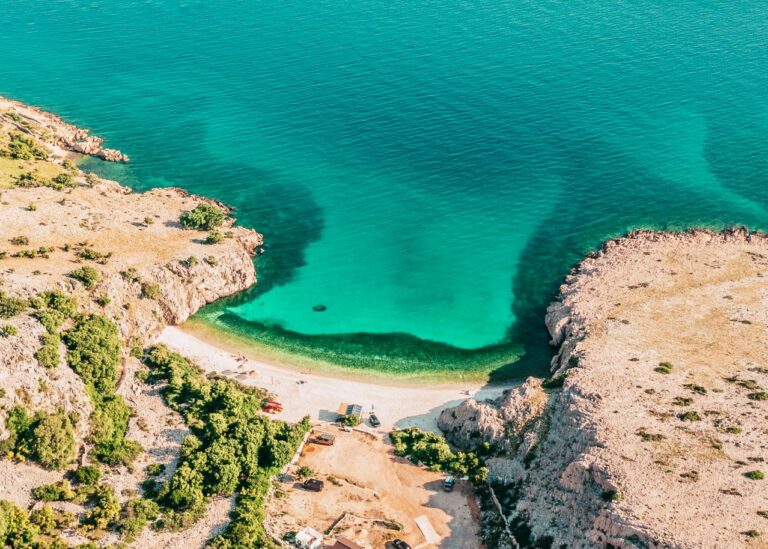 Das Bild zeigt im Vordergrund einen Strand, dahinter türkisfarbenes Wasser, was langsam dunkler wird im Nationalpark Kornaten in Kroatien